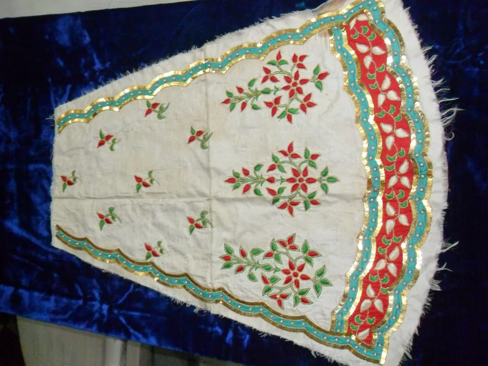 Cream-coloured garment laid flat with red flowers, green leaves and a red-and-green border