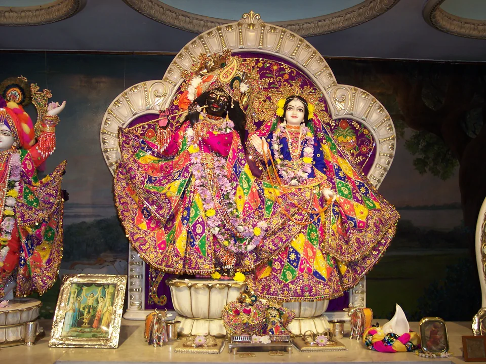 Deities in multicoloured embroidered attire with garlands and a decorative arch behind them