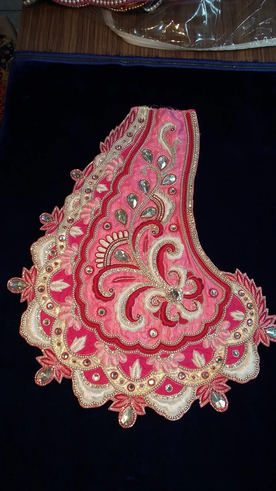 Pink decorative panel with pale scrolling motifs and a scalloped floral edge on a dark surface