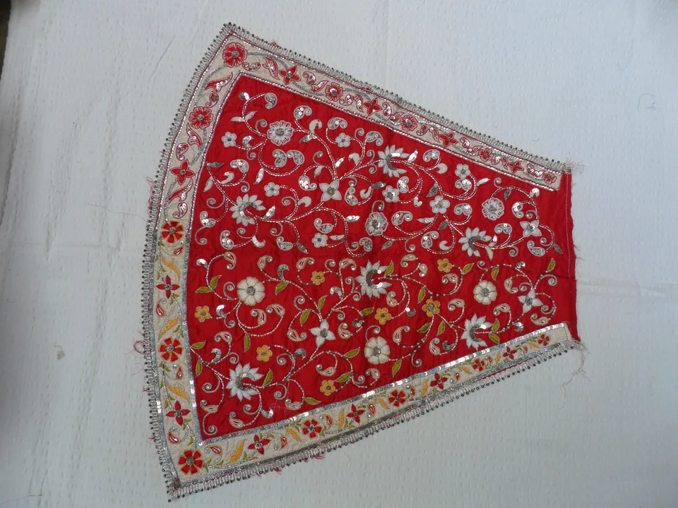 Red shaped fabric panel with pale floral scrolling motifs and an outlined border on a white surface
