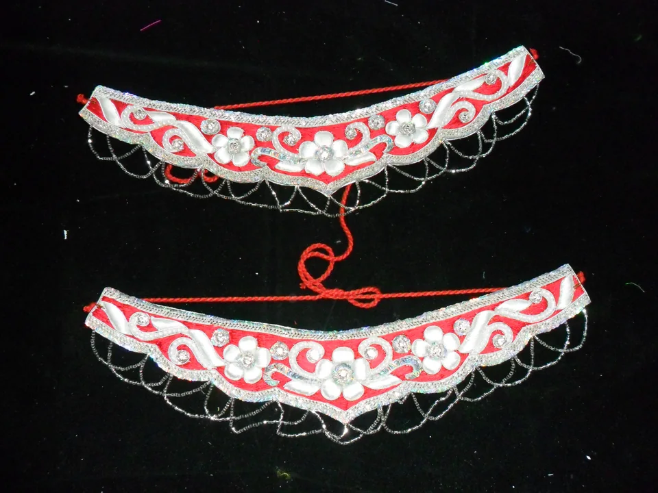 Two red and white embellished curved pieces with thin loops and red cords on a dark surface